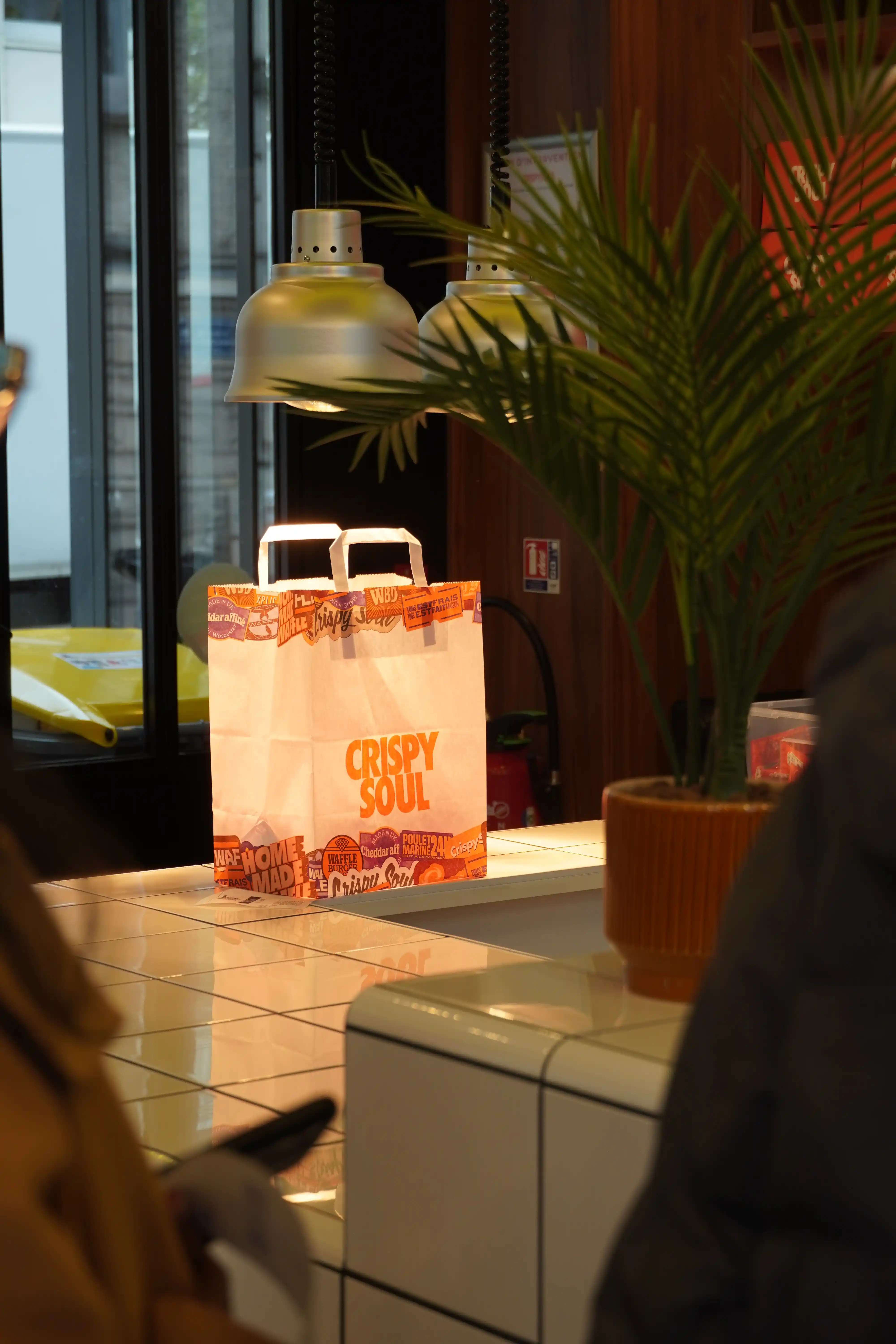 Sac de livraison poulet frit Paris prêt au comptoir CRISPY SOUL à côté d'une plante