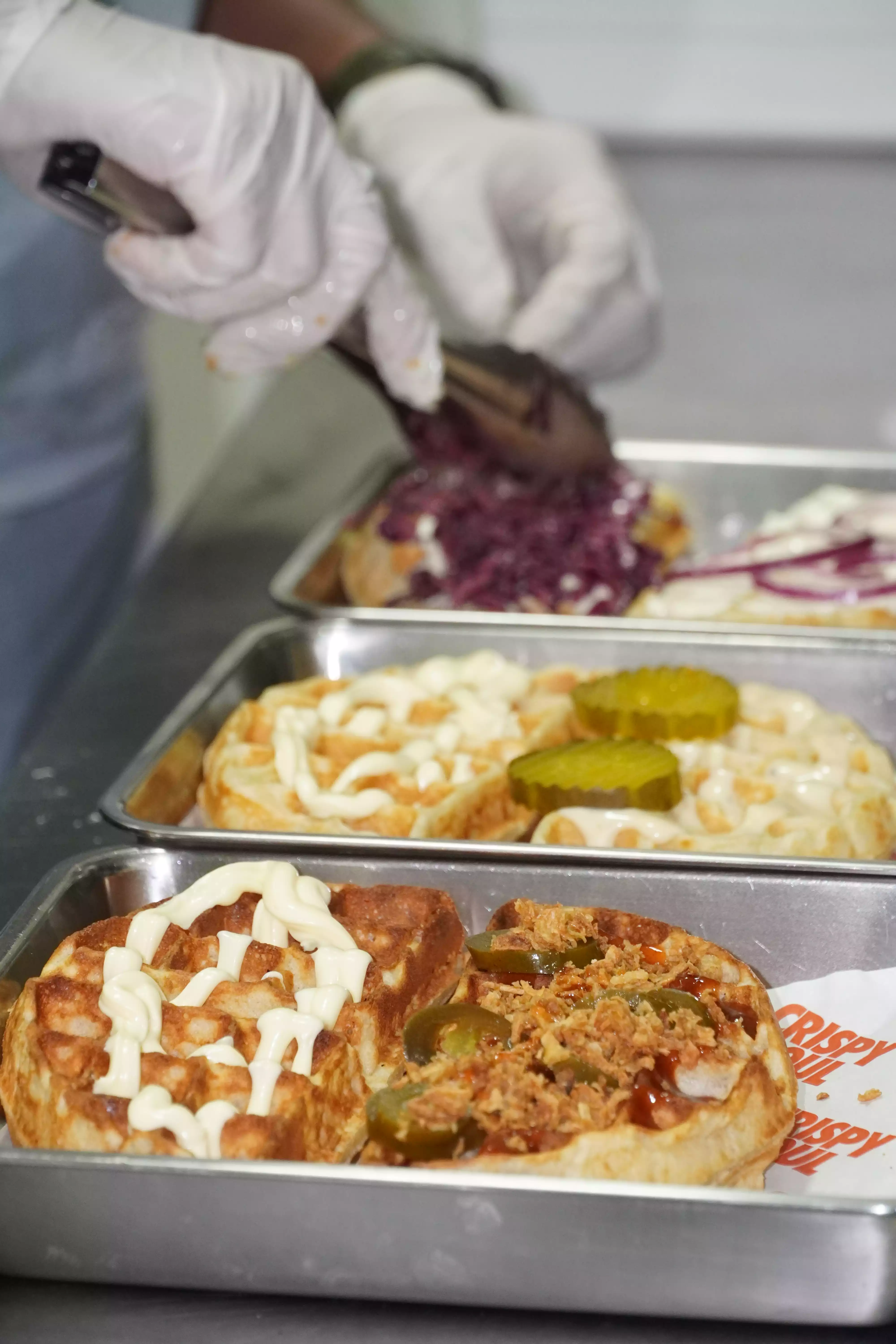 Préparation à la main d'un waffle burger avec poulet frit minute en cuisine CRISPY SOUL